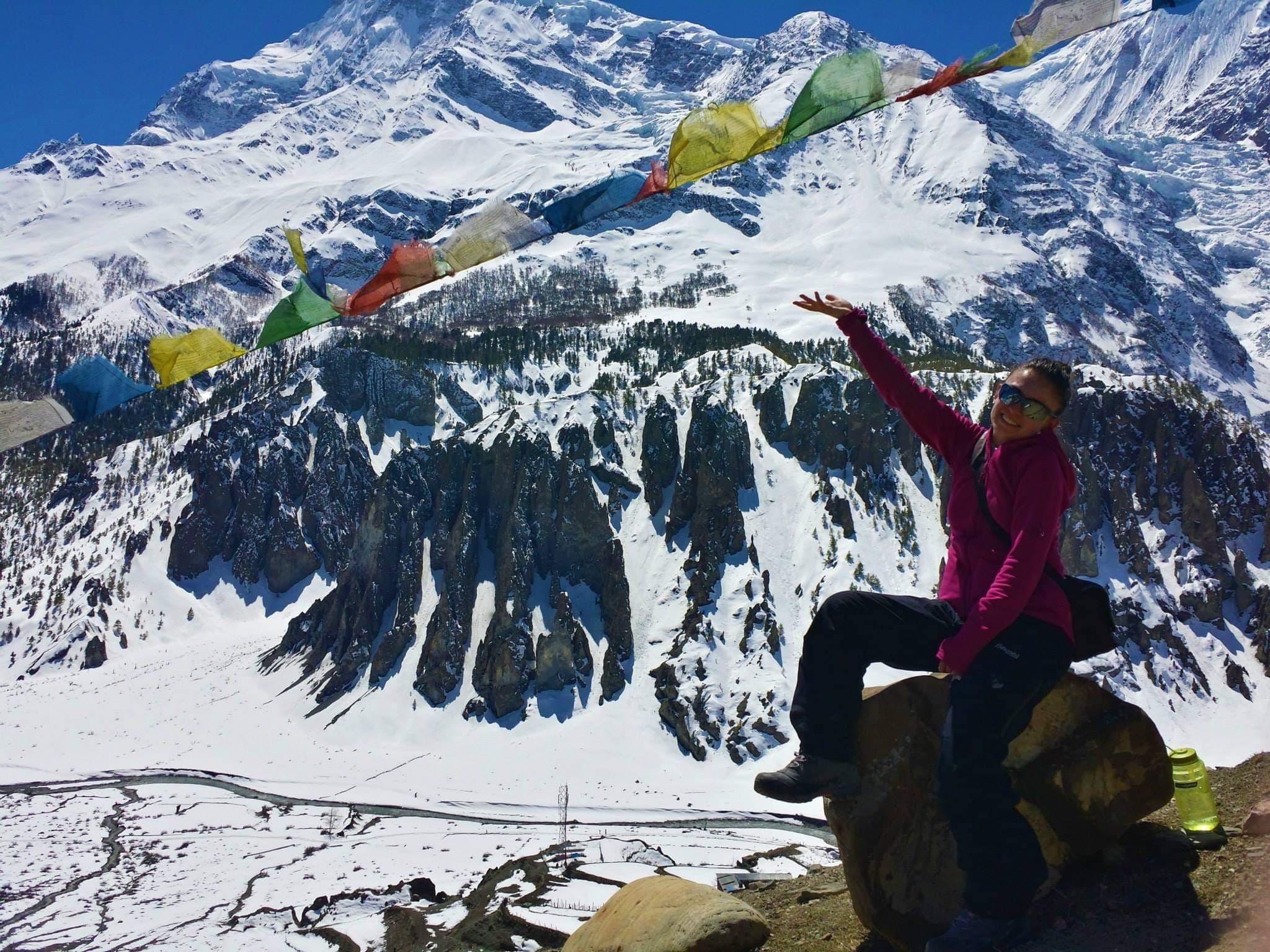 Elis reaching towards prayer flags with snowy Himalayan peaks behind